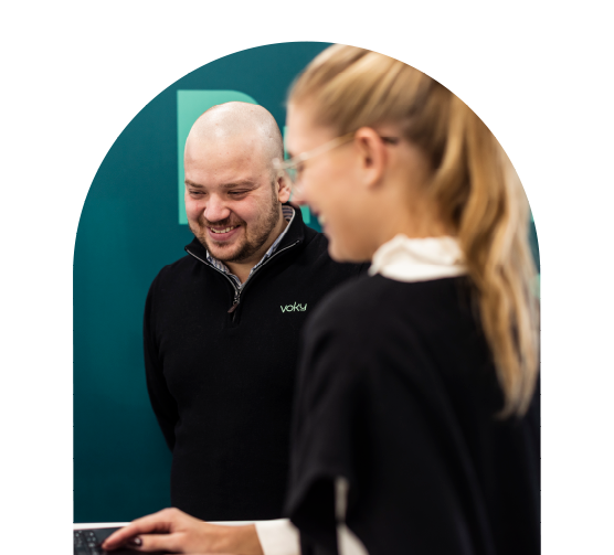 Två leende Voky-anställda som tittar ner på en dator